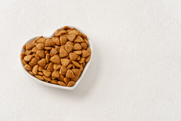 Cat food in a heart-shaped bowl close-up to the left of the copy space