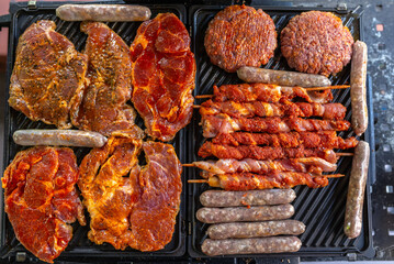 Raw beef and pork meat, sausages on BBQ grill. Top view.