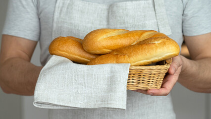 Male hands hold wicker basket with freshly baked french bread baguette and linen towel