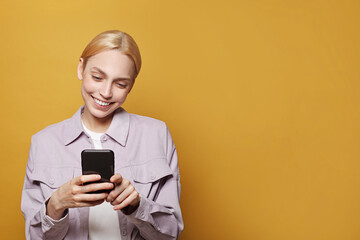 Young woman blonde holds smartphone against vivid yellow studio wall background