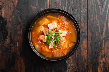 Korean food, kimchi soup with tofu in a ceramic bowl on a wooden background, top view