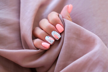 Women - a hand with a beautiful manicure holds a silk fabric. Spring trend, pink nails, drawing on...