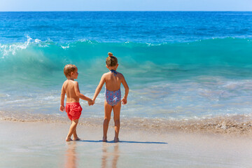 Happy kids have fun in sea surf on white sand beach. Couple of children stand in water pool with...