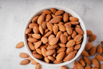 Almonds in white porcelain bowl on white table. Almond concept with copyspace.