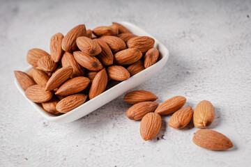 Almonds in white porcelain bowl on white table. Almond concept with copyspace.