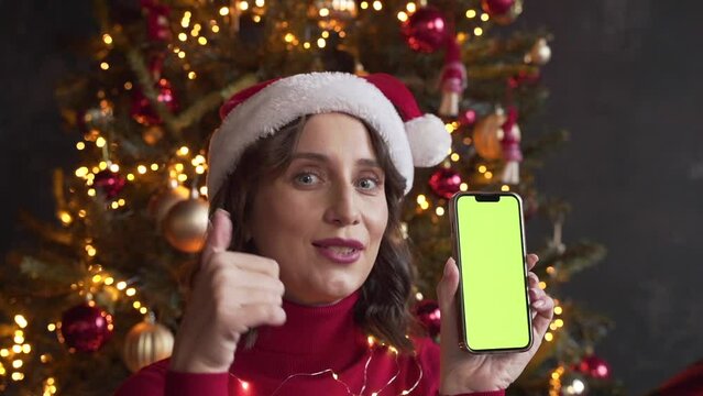Woman in red sweater and Santa's hat holding a mobile phone with a green screen