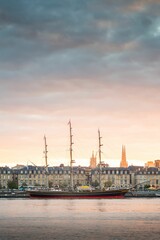 Vertical shot of a ship docked in Garonne River with Bordeaux city in the background during sunset