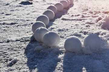 Snowballs lying on the frozen ice nearby glisten in the rays of the sun. Bright sunny day. Winter...