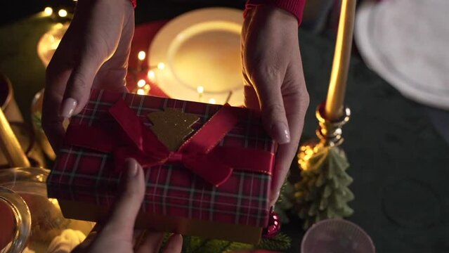 Close up of woman's hands give a gift near the Christmas tree 