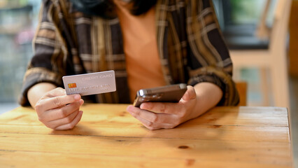 An Asian sitting in the coffee shop, using her smartphone and credit card to pay online bills.