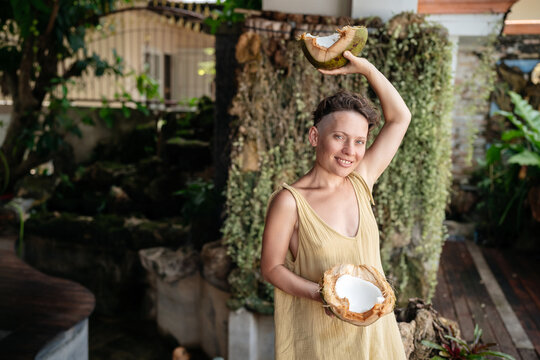 A beautiful young woman with a smile holds halves of a fresh coconut in her hands. Useful natural products for body and organism.