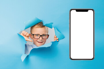 Happy cute businessboy in eyeglasses is having fun on blue background wall, climbs through a hole...
