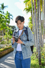 Asian male traveler or freelance photographer adjusting his camera before taking outdoor picture.