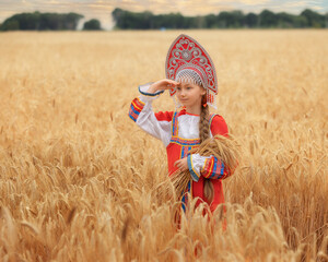 Littl girl kid in Russian national sarafan and a kokoshnik standing in a golden wheat field in...