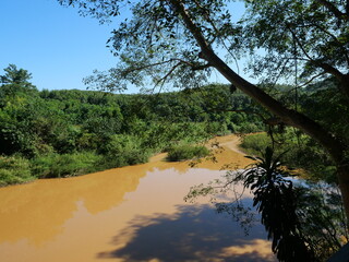 Brown water is flowing slowly in the Nan River in the valley and forest full of green tree with blue sky in background, Thailand