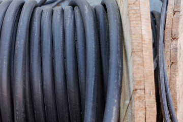 Large spool of black thick electrical wire or cable. Wooden reel with electrical industrial wires at a construction site. 