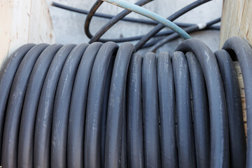 Large spool of black thick electrical wire or cable. Wooden reel with electrical industrial wires at a construction site. 
