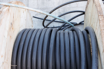 Large spool of black thick electrical wire or cable. Wooden reel with electrical industrial wires at a construction site. 
