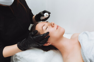 A woman undergoes a cosmetic procedure at the salon spa. The cosmetologist puts the cream on the...