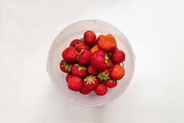 Ripe red strawberries in a round white dish on a white background.