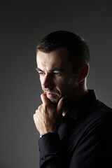 Portrait of pensive man in a black shirt on a dark background. Young caucasian dark-haired man