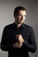 Fototapeta na wymiar Portrait of pensive man in a black shirt on a dark background. Young caucasian dark-haired man