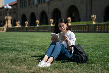 happy asian taiwanese college girl book lover having fun learning while relaxing on the grass with folding knees on school campus in California usa