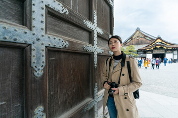 nostalgic asian Japanese female photographer gazing into distance in contemplation by giant historic entrance gate at Motorikyu Nijyojo nijo castle in Kyoto japan