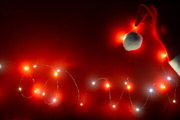 New year banner with Santa hat and lights garland on red background. Card with a magical holiday...