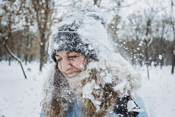 Fototapeta na wymiar Close up outdoor winter portrait of woman in winter clothes. Candid portrait of young woman in winter time. Mom playing snowballs, walking under snow. Outdoors winter activities for adults, family.