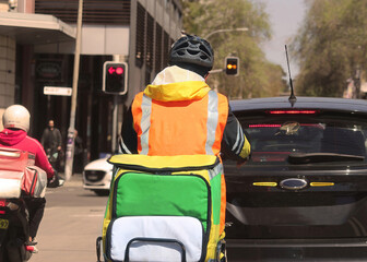 A food courier wearing hi vis clothing riding a motor bike in traffic
