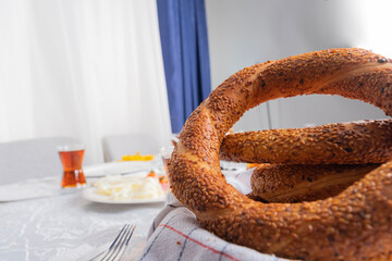 Close up photo of Turkish bagel called Simit. Traditional Turkish breakfast bakery fast food. Glass of tea and table setup blurred background. Home morning routine. Copy space area.