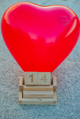 Calendario de madera reciclada que marca el 14 de febrero, Día de San Valentín en sus cubos con un globo en forma de corazón en el fondo.