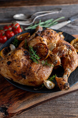 Roasted lemon chicken legs with thyme and garlic on a dark plate on wooden table
