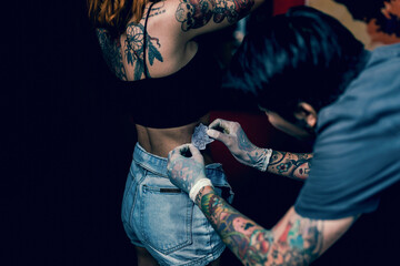 Close-up hands of master Tattoo artist in white gloves sticking paper with pattern on client hand on a girl's waist, in a modern studio lowlight.