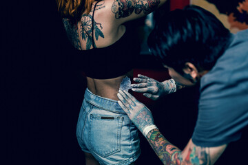 Close-up hands of master Tattoo artist in white gloves sticking paper with pattern on client hand on a girl's waist, in a modern studio lowlight.