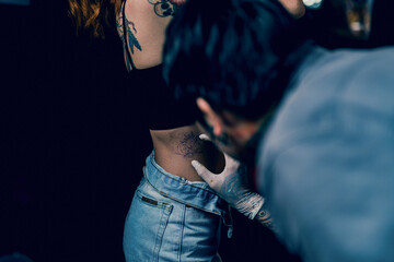 Close-up hands of master Tattoo artist in white gloves sticking paper with pattern on client hand on a girl's waist, in a modern studio lowlight.