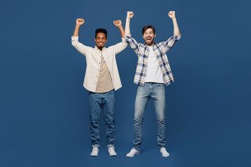 Obraz premium Full size young two friends men 20s wear white casual shirts together doing winner gesture celebrate clenching fists say yes isolated plain dark royal navy blue background. People lifestyle concept.