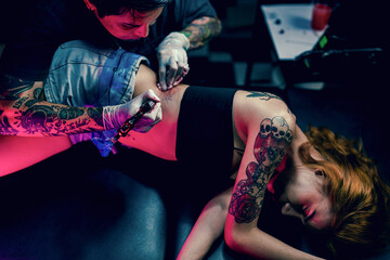 Professional tattooist makes the tattoo on a girl waist, focusing on tattoo machines in a modern...