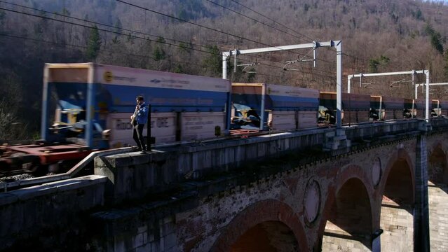 Guitar Player on a Bridge With a Moving Train Behind Drone Shot