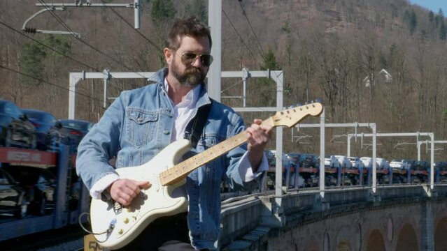 A Moving Train on a Bridge Behind a Guitar Player