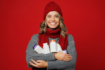 Young smiling woman wear grey sweater scarf hat hold many bottles with drugs pills isolated on...