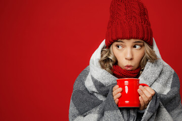 Close up young woman wearing scarf hat wrapped in grey plaid drink hot tea look aside on area...
