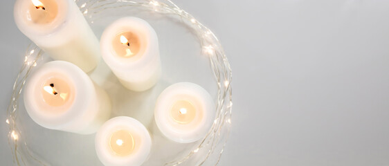 Large burning candles and Christmas garland on a white background. Side view, space for text.