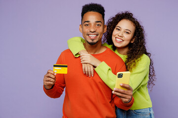 Young couple two friends family man woman of African American ethnicity in casual clothes together use mobile cell phone credit bank card do online shopping isolated on plain light purple background