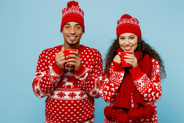 Merry young couple two man woman wear red Christmas sweater Santa hat posing hold in hand cup of...