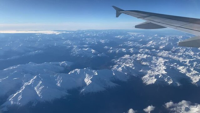 Windows Plane Aerial View Of Flight Over Alps Between Clouds. Stunning Blue Landscape, White Snow On The Top Of Mountains.