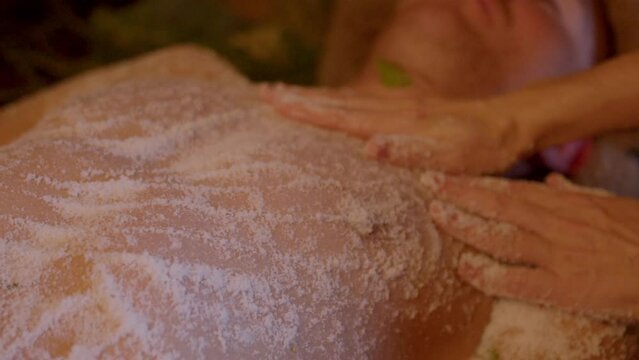 Slow, relaxing, soothing hand movements of masseuse rubbing aromatic sea salt over mans body in sauna. Therapeutic procedures in Finnish sauna - scrub, peeling.