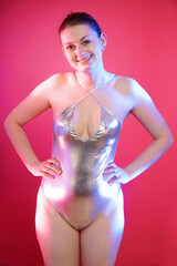 Beautiful cheerful woman posing in silver metallic one piece swimsuit in front of pink background...