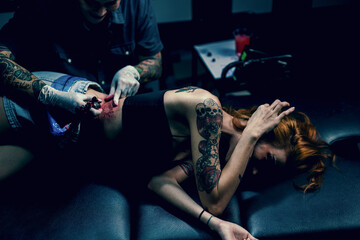 Professional tattooist makes the tattoo on a girl waist, focusing on tattoo machines in a modern studio lowlight.